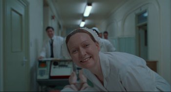 Movie still from “Velvet Goldmine” (1998), directed by Todd Haynes – A woman in a white robe smiles for the camera; Medium shot, High angle