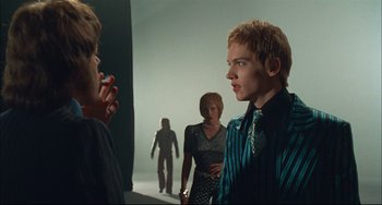 Movie still from “Velvet Goldmine” (1998), directed by Todd Haynes – A group of people standing in front of each other in a room; Medium shot, Over the shoulder angle
