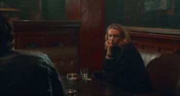 Movie still from “Velvet Goldmine” (1998), directed by Todd Haynes – A woman sitting at a table with a glass in front of her face; Medium shot, Over the shoulder angle