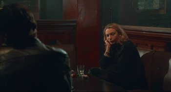 Movie still from “Velvet Goldmine” (1998), directed by Todd Haynes – A woman sitting at a table with a glass in front of her; Medium shot, Over the shoulder angle