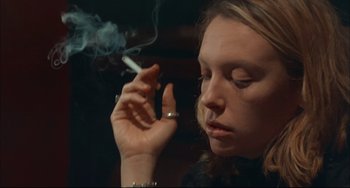 Movie still from “Velvet Goldmine” (1998), directed by Todd Haynes – A woman smoking a cigarette in a dark room; Close Up shot, Low angle