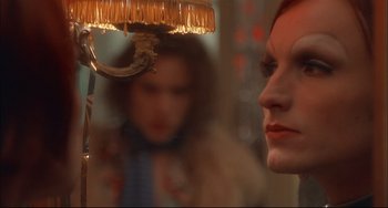 Movie still from “Velvet Goldmine” (1998), directed by Todd Haynes – A woman looking into a mirror while a man looks on; Close Up shot, Over the shoulder angle