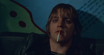 Movie still from “Velvet Goldmine” (1998), directed by Todd Haynes – A man smoking a cigarette while sitting in a chair; Close Up shot, Low angle