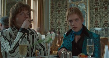 Movie still from “Velvet Goldmine” (1998), directed by Todd Haynes – Two people sitting at a table in front of a vase of flowers; Medium shot, Low angle