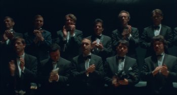Movie still from “Velvet Goldmine” (1998), directed by Todd Haynes – A group of men in suits and ties clapping in front of a wall; Wide shot, Low angle