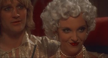 Movie still from “Velvet Goldmine” (1998), directed by Todd Haynes – A woman with white curly hair wearing a white wig; Close Up shot, Over the shoulder angle