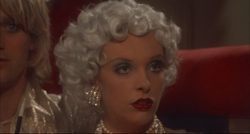 Movie still from “Velvet Goldmine” (1998), directed by Todd Haynes – A person wearing a wig and jewelry; Close Up shot, Over the shoulder angle
