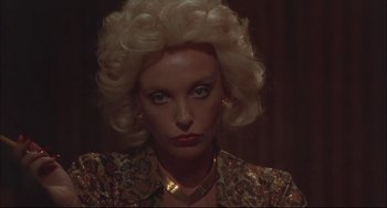 Movie still from “Velvet Goldmine” (1998), directed by Todd Haynes – A woman with blonde curly hair wearing a gold necklace; Close Up shot, Low angle