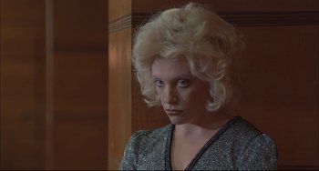 Movie still from “Velvet Goldmine” (1998), directed by Todd Haynes – A woman with blonde curly hair wearing a silver top; Close Up shot, Low angle