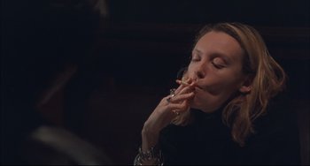 Movie still from “Velvet Goldmine” (1998), directed by Todd Haynes – A woman is smoking a cigarette in a dark room; Close Up shot, High angle