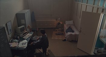 Movie still from “Velvet Goldmine” (1998), directed by Todd Haynes – A person sitting at a desk in a room; Wide shot, High angle