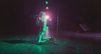 Movie still from “Velvet Goldmine” (1998), directed by Todd Haynes – A person sitting on the ground holding a microphone; Wide shot, High angle