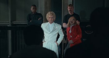 Movie still from “Velvet Goldmine” (1998), directed by Todd Haynes – A group of people standing next to each other in front of a mirror; Medium shot, Low angle