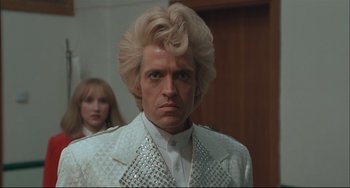 Movie still from “Velvet Goldmine” (1998), directed by Todd Haynes – A man in a white suit with a blonde wig; Close Up shot, Low angle