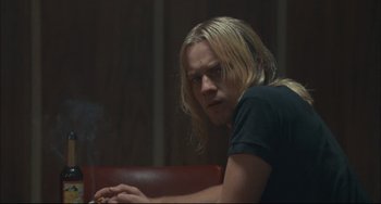 Movie still from “Velvet Goldmine” (1998), directed by Todd Haynes – A man with long blonde hair sitting in front of a laptop computer; Medium shot, Over the shoulder angle