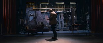 Movie still from “Venus in Fur” (2013), directed by Roman Polanski – A man standing on a skateboard in a dark room; Wide shot, Low angle