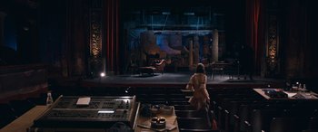 Movie still from “Venus in Fur” (2013), directed by Roman Polanski – A woman sitting in front of a stage with a microphone; Extreme Wide shot, High angle