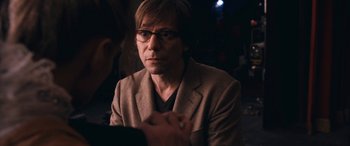 Movie still from “Venus in Fur” (2013), directed by Roman Polanski – A man wearing glasses and a jacket is sitting in a dark room; Close Up shot, Over the shoulder angle