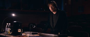 Movie still from “Venus in Fur” (2013), directed by Roman Polanski – A man sitting at a table in front of a microphone; Medium shot, High angle