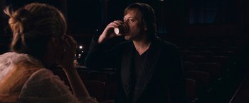 Movie still from “Venus in Fur” (2013), directed by Roman Polanski – A man drinking from a cup while sitting at a table; Medium shot, Over the shoulder angle