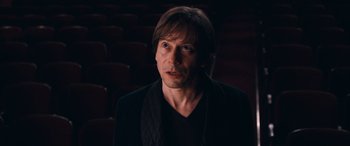 Movie still from “Venus in Fur” (2013), directed by Roman Polanski – A man in a black jacket is in a dark room; Close Up shot, High angle