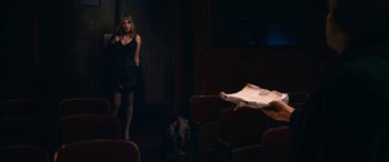 Movie still from “Venus in Fur” (2013), directed by Roman Polanski – A woman standing in front of an audience in a dark room; Wide shot, Over the shoulder angle
