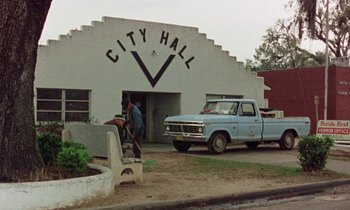 Movie still from “Vernon, Florida” (1981), directed by Errol Morris – Two men standing in front of a city hall building; Extreme Wide shot, Low angle