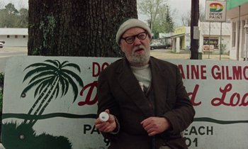 Movie still from “Vernon, Florida” (1981), directed by Errol Morris – An older man holding a cigarette in front of a tree; Medium shot, Low angle