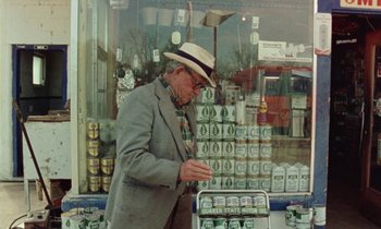 Movie still from “Vernon, Florida” (1981), directed by Errol Morris – An older man in a hat and a suit is looking at a case of beer; Medium shot, Low angle