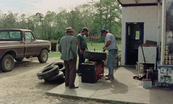 Movie still from “Vernon, Florida” (1981), directed by Errol Morris – A group of men standing next to a truck; Wide shot, High angle