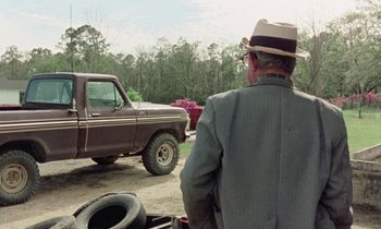 Movie still from “Vernon, Florida” (1981), directed by Errol Morris – An older man wearing a hat looking at an old truck; Wide shot, Over the shoulder angle