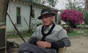 Movie still from “Vernon, Florida” (1981), directed by Errol Morris – An old man sitting in a chair in front of a house; Medium shot, Low angle