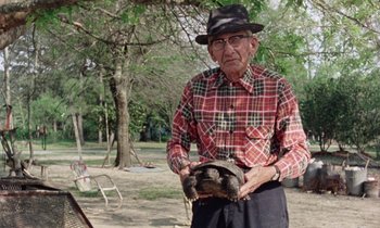 Movie still from “Vernon, Florida” (1981), directed by Errol Morris – An older man holding a turtle in a park; Medium shot, Low angle