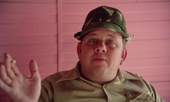 Movie still from “Vernon, Florida” (1981), directed by Errol Morris – A man wearing a camouflage hat with a pen in his hand; Close Up shot, Low angle