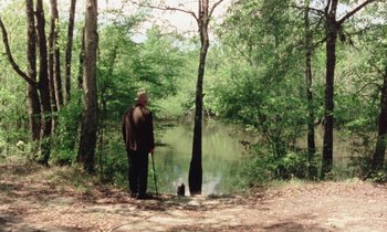 Movie still from “Vernon, Florida” (1981), directed by Errol Morris – An old man standing next to a body of water; Wide shot, High angle