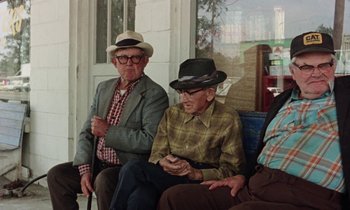 Movie still from “Vernon, Florida” (1981), directed by Errol Morris – Two older men sitting on a bench wearing hats; Medium shot, Low angle