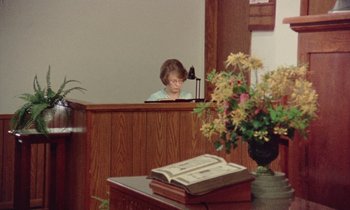 Movie still from “Vernon, Florida” (1981), directed by Errol Morris – A woman sitting at a desk in a church; Wide shot, High angle