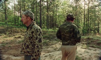 Movie still from “Vernon, Florida” (1981), directed by Errol Morris – Two men standing in a wooded area wearing camouflage clothing; Wide shot, Over the shoulder angle
