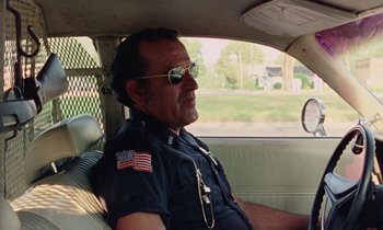 Movie still from “Vernon, Florida” (1981), directed by Errol Morris – A police officer sitting in the back seat of a car; Medium shot, Low angle