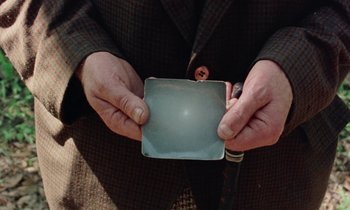 Movie still from “Vernon, Florida” (1981), directed by Errol Morris – An older man holding a metal object in his hands; Extreme Close Up shot, Overhead angle