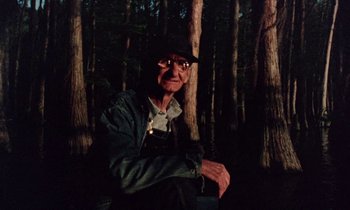 Movie still from “Vernon, Florida” (1981), directed by Errol Morris – An older man in a forest with trees; Medium shot, Low angle