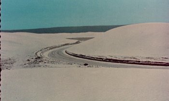Movie still from “Vernon, Florida” (1981), directed by Errol Morris – A road in the middle of a snow covered field; Extreme Wide shot, High angle