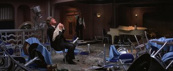 Movie still from “Victor/Victoria” (1982), directed by Blake Edwards – A man sitting on a chair in a room with broken chairs; Wide shot, High angle