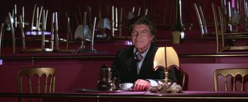 Movie still from “Victor/Victoria” (1982), directed by Blake Edwards – An older man sitting at a table with a cup of coffee; Medium shot, Low angle