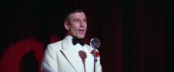 Movie still from “Victor/Victoria” (1982), directed by Blake Edwards – A man in a white suit is holding a microphone; Close Up shot, Low angle