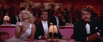 Movie still from “Victor/Victoria” (1982), directed by Blake Edwards – A group of people sitting at a table in front of a lamp; Medium shot, Low angle