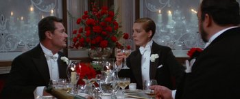 Movie still from “Victor/Victoria” (1982), directed by Blake Edwards – A woman in a tuxedo drinking wine at a formal dinner; Medium shot, Over the shoulder angle