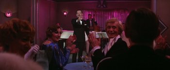 Movie still from “Victor/Victoria” (1982), directed by Blake Edwards – A group of people sitting at a table clapping; Medium shot, Over the shoulder angle