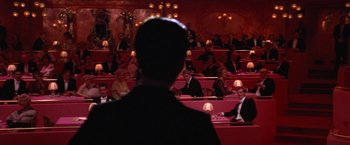 Movie still from “Victor/Victoria” (1982), directed by Blake Edwards – A man standing in front of a group of people in a room; Wide shot, Over the shoulder angle
