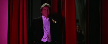 Movie still from “Victor/Victoria” (1982), directed by Blake Edwards – A man in a tuxedo sitting in front of a red curtain; Medium shot, Low angle